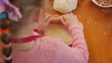 Küçük kız hamur pizzası yuvarlıyor.