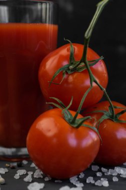 Kırmızı domatesli taze domates suyu ve koyu arkaplanda kaba tuz.