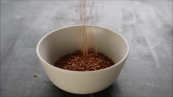 El trigo sarraceno se vierte en un tazón sobre una mesa oscura — Vídeo de stock