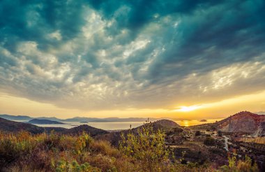 Dağlar ve deniz ve dramatik bulutların üstünde renkli gün batımı görünümü