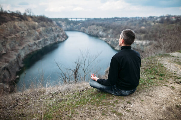 Man meditating on rocky cliff with river view