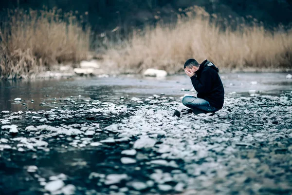Portret człowieka podkreślił rozpacz siedzący na rzece. — Zdjęcie stockowe