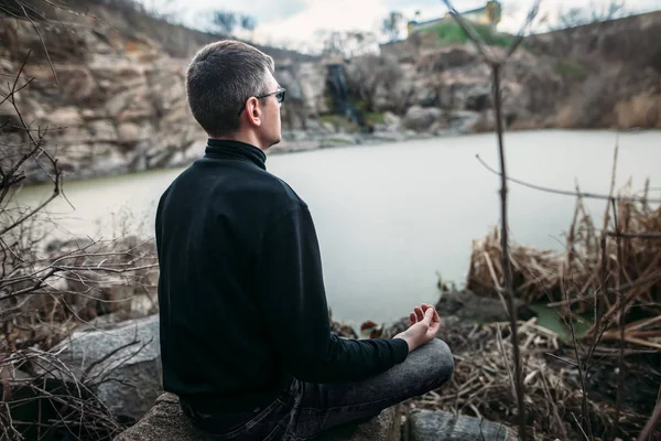 Nehir Manzaralı kayalık uçurum üzerinde meditasyon adam — Stok fotoğraf