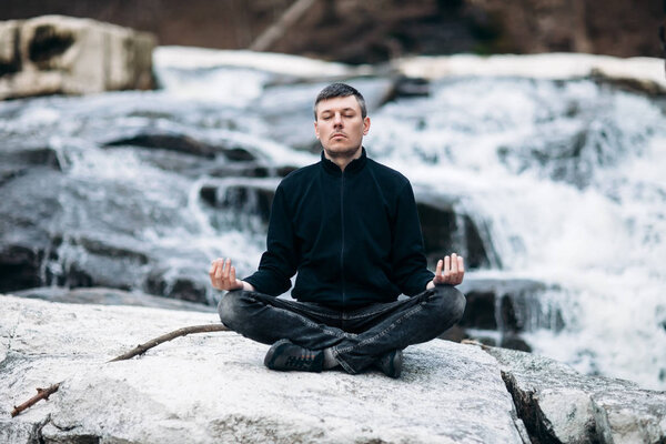 Man meditating in Lotus Pose on waterfall