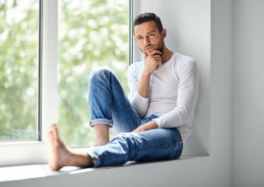 Pencere pervazına üzerinde oturan düşünceli adam