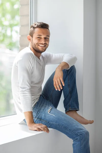 Smiling man relaxing on window sill — Stok fotoğraf