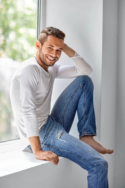 Feliz hombre sonriente relajándose en alféizar ventana —  Fotos de Stock