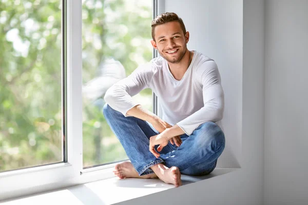 Smiling man sitting on window sill — ストック写真