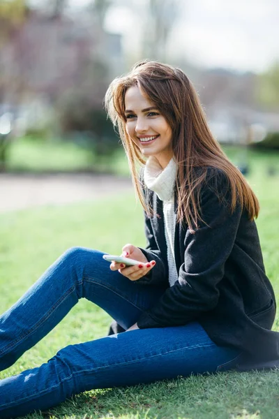 Mooie lachende vrouw met telefoon zittend op een gras in de natuur — Stockfoto