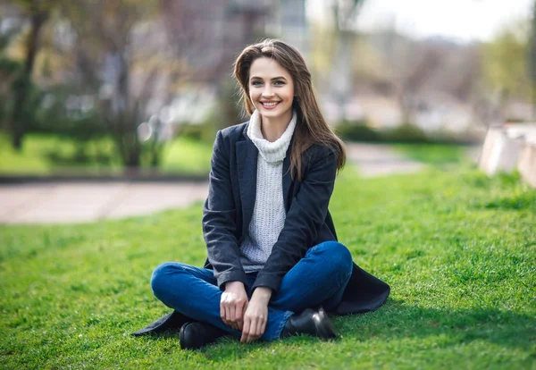 Mulher sorridente bonita sentada em uma grama ao ar livre — Fotografia de Stock