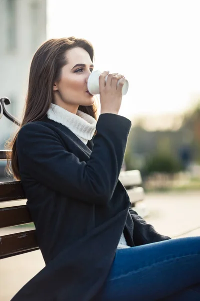 Kobieta, picie kawy siedząc na ławce — Zdjęcie stockowe