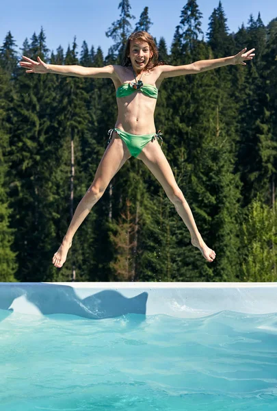 Girl joyfully jumps into swimming pool in shape of star on background of picturesque forest. Child in swimsuit dives into water outdoors. Rest, play, entertainment, weekend concept