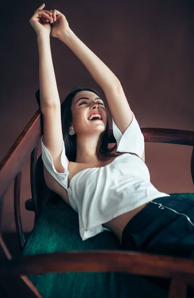 ソファで 手を頭の後ろに曲がっている笑っている若い女性 — ストック写真
