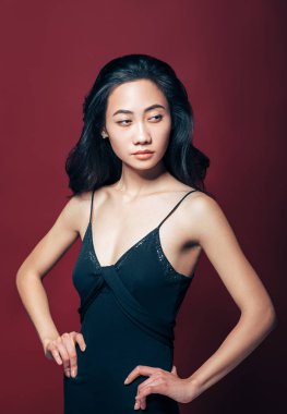 Kendine güvenen güzel Asyalı kız siyah elbiseli kalça üzerinde eller. Güzel moda model portre