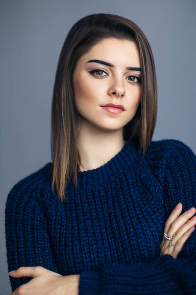 Портрет молодой чувственной женщины со скрещенными руками на сером фоне
