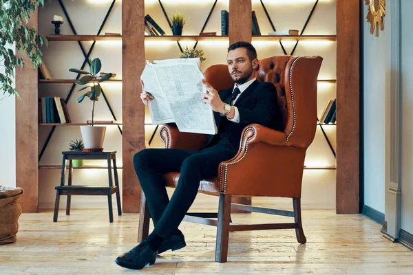 自信的年轻商人坐在扶手椅上看报纸和最新消息 — 图库照片