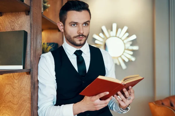 穿着雅致西服的英俊年轻人正在读一本现代豪华室内装潢的书 — 图库照片