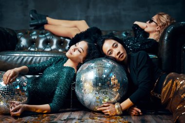 Çok ırklı genç kadınlar partiden sonra rahat bir şekilde yere ve kanepeye uzanırlar.