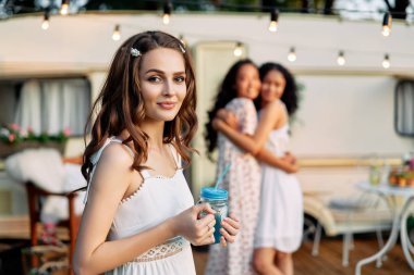Piknik sırasında karavanın ve arka plandaki arkadaşlarının yanında güzel genç kadın portresi. Tatil, gezi ve tatil konsepti