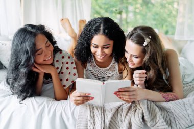 Gülümseyen çok ırklı kadınlar birlikte eğleniyorlar ve karavanın içinde kitap okuyarak eğleniyorlar.. 