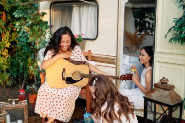 Güler yüzlü, gitarlı kadınlar yaz tatili sırasında karavanın yanında birlikte eğleniyorlar..