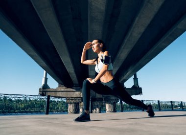 Sportif kadın koşucu egzersiz yapmadan önce ısınmak ve diğer tarafa bakmak için bacaklarını açıyor. Kentsel çalışma ve çalışma konsepti                 