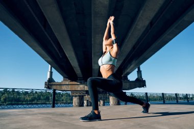 Genç sporcu kadın yoga yapıyor. Asana Savaşçısı. Endüstriyel köprünün altında poz veriyor. Yoga, refah ve sağlıklı bir yaşam tarzı. Virabhadrasana        