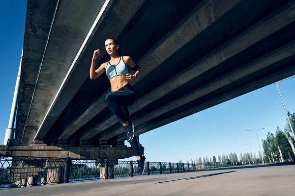 一个身材瘦小的女人在城桥下面跑来跑去 穿着运动服的漂亮女人 动态运动 — 图库照片