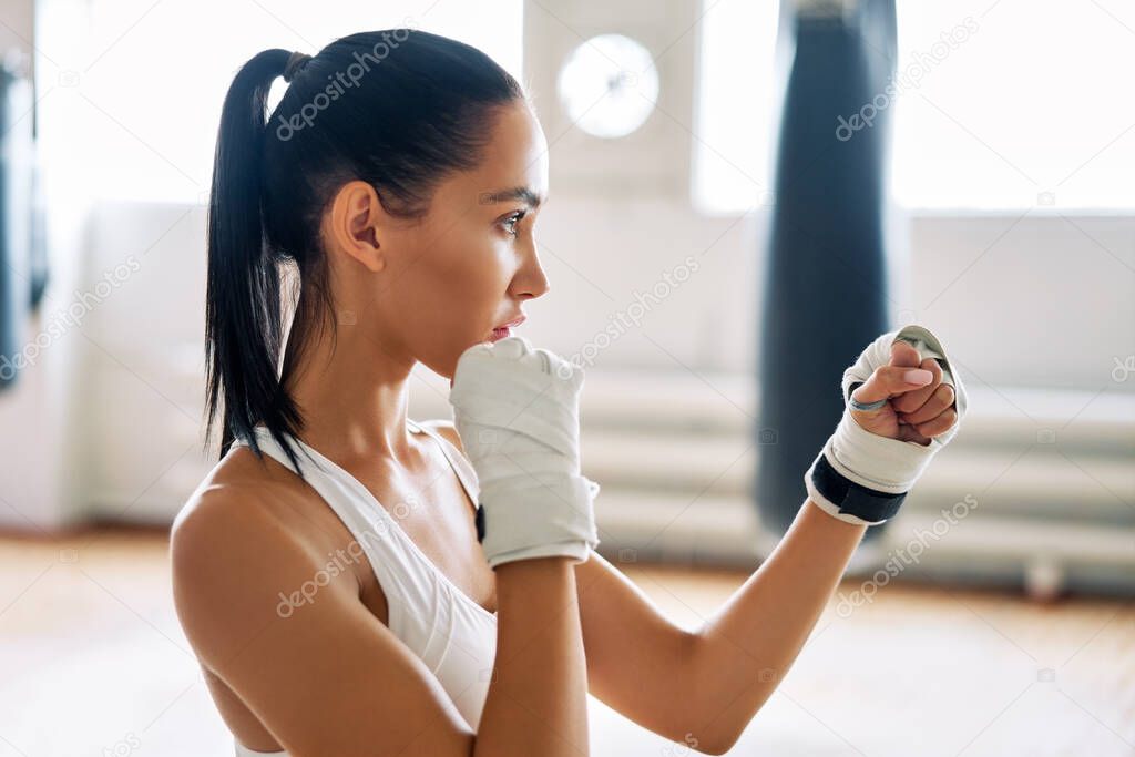 Young boxer woman posing in combat stance in gym. Sporty female ready for fight                 