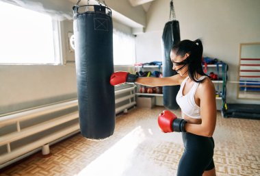 Bayan boksör spor salonunda büyük bir kum torbasına vuruyor. Kadın boks stüdyosunda yumruk pratiği yapıyor.                 
