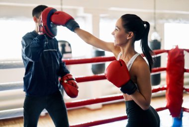 Bayan boksör, spor salonunda kişisel antrenörünün boks eldivenlerini tutuyor. Sağlıklı yaşam tarzı kavramı              