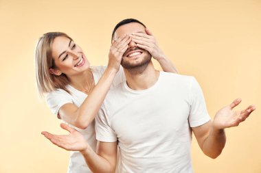 Bil bakalım kim? Onun için sürpriz. Güzel genç bir kadın, sarı arka planda izole edilmiş erkek arkadaşının gözlerini kapatıyor.