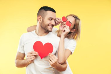 Aşık mutlu çift sarı arka planda kağıt kalplerle eğlenir. İlişki ve romantik konsept.