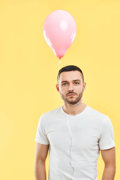 一个奇怪的年轻人 脖子上挂着粉色气球 背景是黄色的工作室 — 图库照片