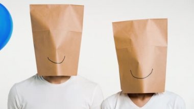 Kafasında gülen kağıt poşet olan ve elinde balon tutan bir çift adam ve kadın. Şaka, eğlence, anonim konsept