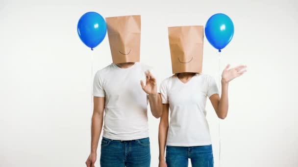 挨拶の手を振って頭の上に紙袋を手に若いカップルや気球を保持します 楽しさ 匿名の概念 — ストック動画