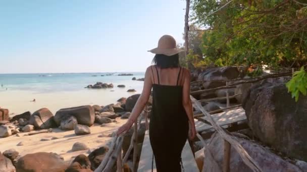 Vista trasera de una joven caminando sobre un puente de madera en una isla tropical — Vídeos de Stock