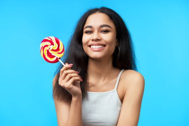 Mavi arka planda renkli lolipopu olan mutlu, güzel siyahi kadın. Tatlı yemek, zevk, eğlence konsepti