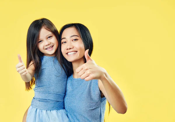 Mãe feliz e sua filha criança mostrando polegares para cima no fundo amarelo — Fotografia de Stock