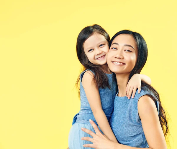 Mãe feliz e sua filha criança abraçando no fundo amarelo . — Fotografia de Stock