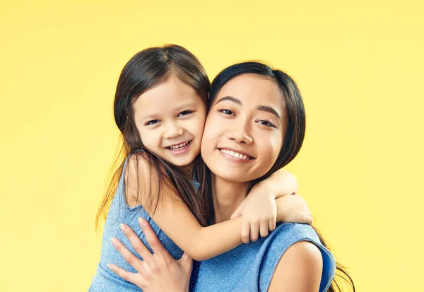 Mãe feliz e sua filha criança abraçando no fundo amarelo . — Fotografia de Stock