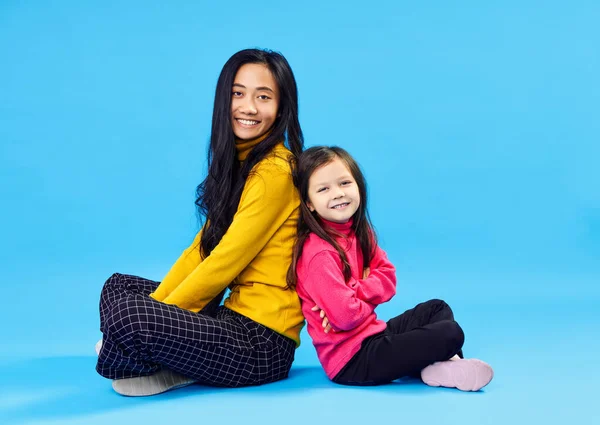 Glad leende mor och hennes lilla söta dotter poserar på blå bakgrund — Stockfoto