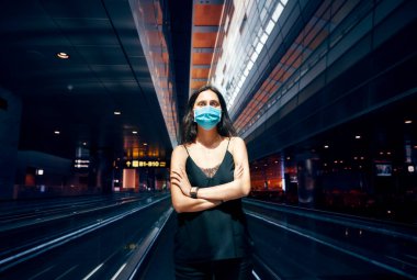 Modern alışveriş merkezinde ya da havaalanında poz veren koruma maskeli kadın.