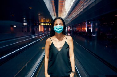 Modern alışveriş merkezinde ya da havaalanında poz veren koruma maskeli kadın.