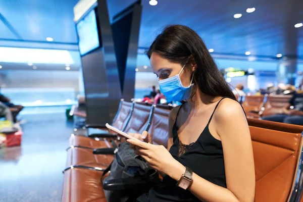 Vrouw in virus bescherming gezichtsmasker met behulp van een smartphone zitten in lege luchthaven — Stockfoto