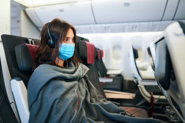 Vrouw in virus bescherming gezichtsmasker zittend in leeg vliegtuig — Stockfoto