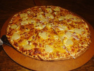Ananas ve pastırma dilimli yuvarlak pizza Topingler bir yuvarlak Düz ahşap plakalı servis, bit