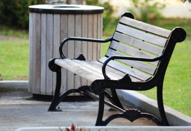 Parkta koldayan rahat bir ahşap bank, yanında ahşap bir çöp kutusu ile