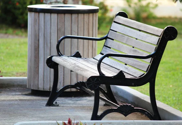 Parkta koldayan rahat bir ahşap bank, yanında ahşap bir çöp kutusu ile