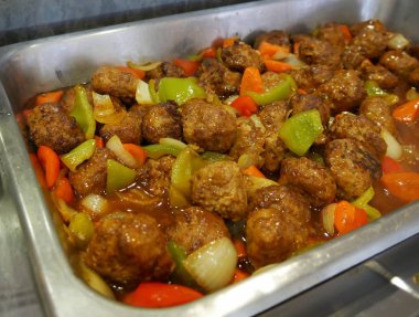 Dikdörtgen metal tepside dilimlenmiş soğan, yeşil ve kırmızı biber ile soslu köfte